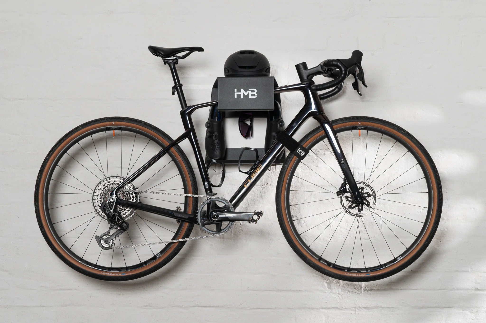 The Hold My Bike (HMB) Ultimate set in black: A horizontally aligned gravel bike on the wall, perfectly balanced thanks to the innovative HMB tilt mechanism for indoor storage.