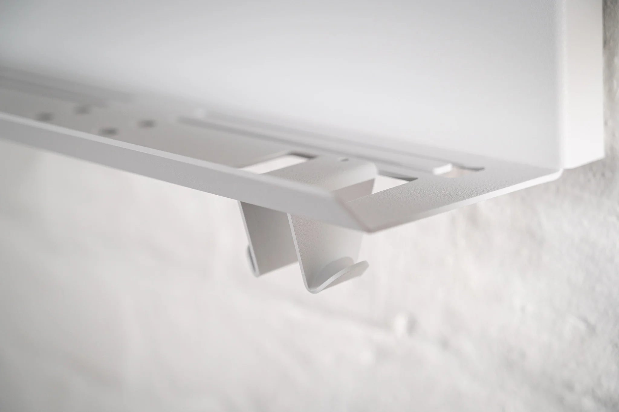 Macro shot of the precision-engineered lower gear shelf on the white HMB Ultimate wall organizer, highlighting the integrated hooks and laser-cut slots designed for cycling jerseys and accessories.