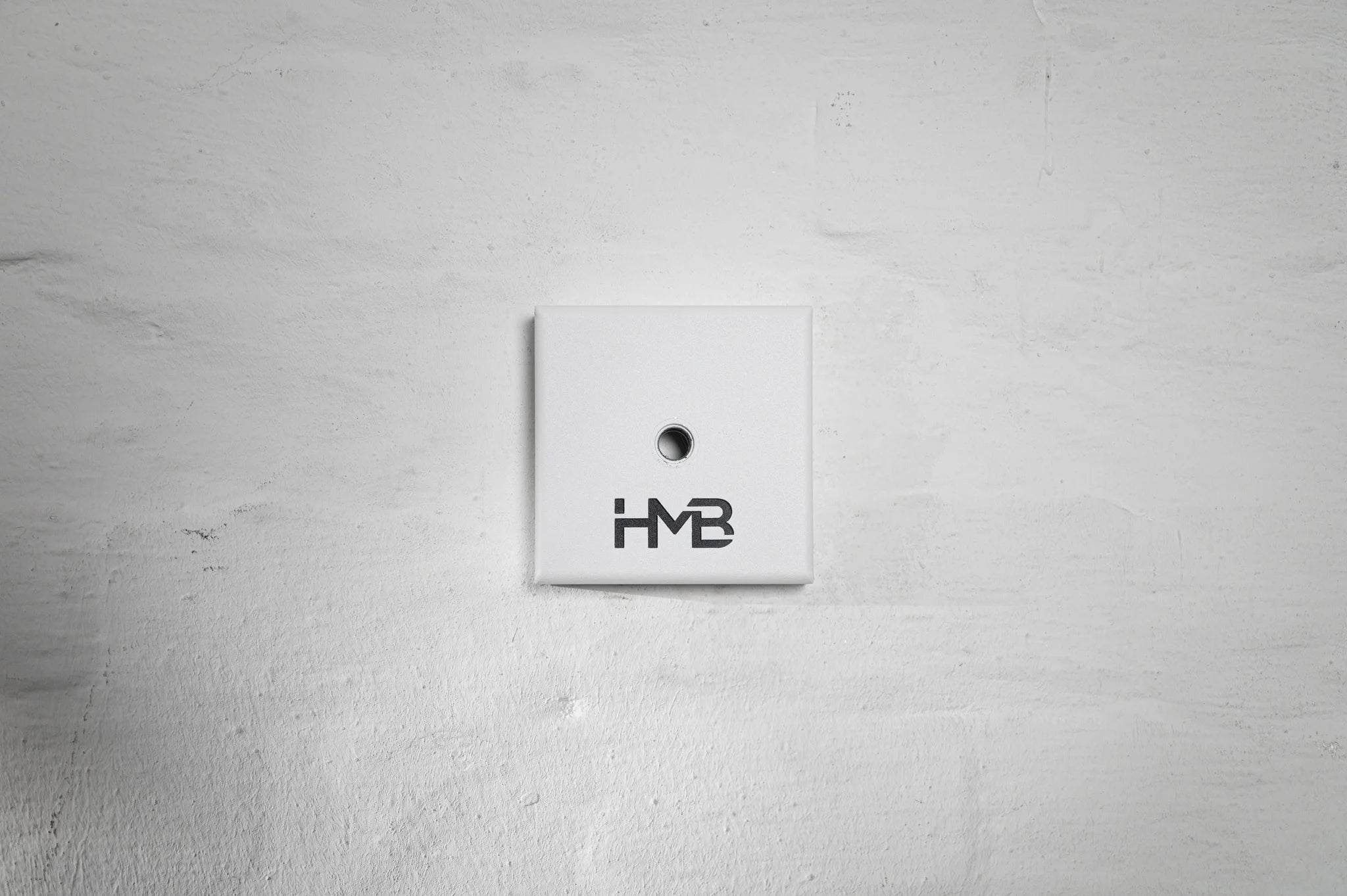 The minimalist white Hold My Bike (HMB) wheel mount featuring bold logo branding for a clean and modern indoor design.