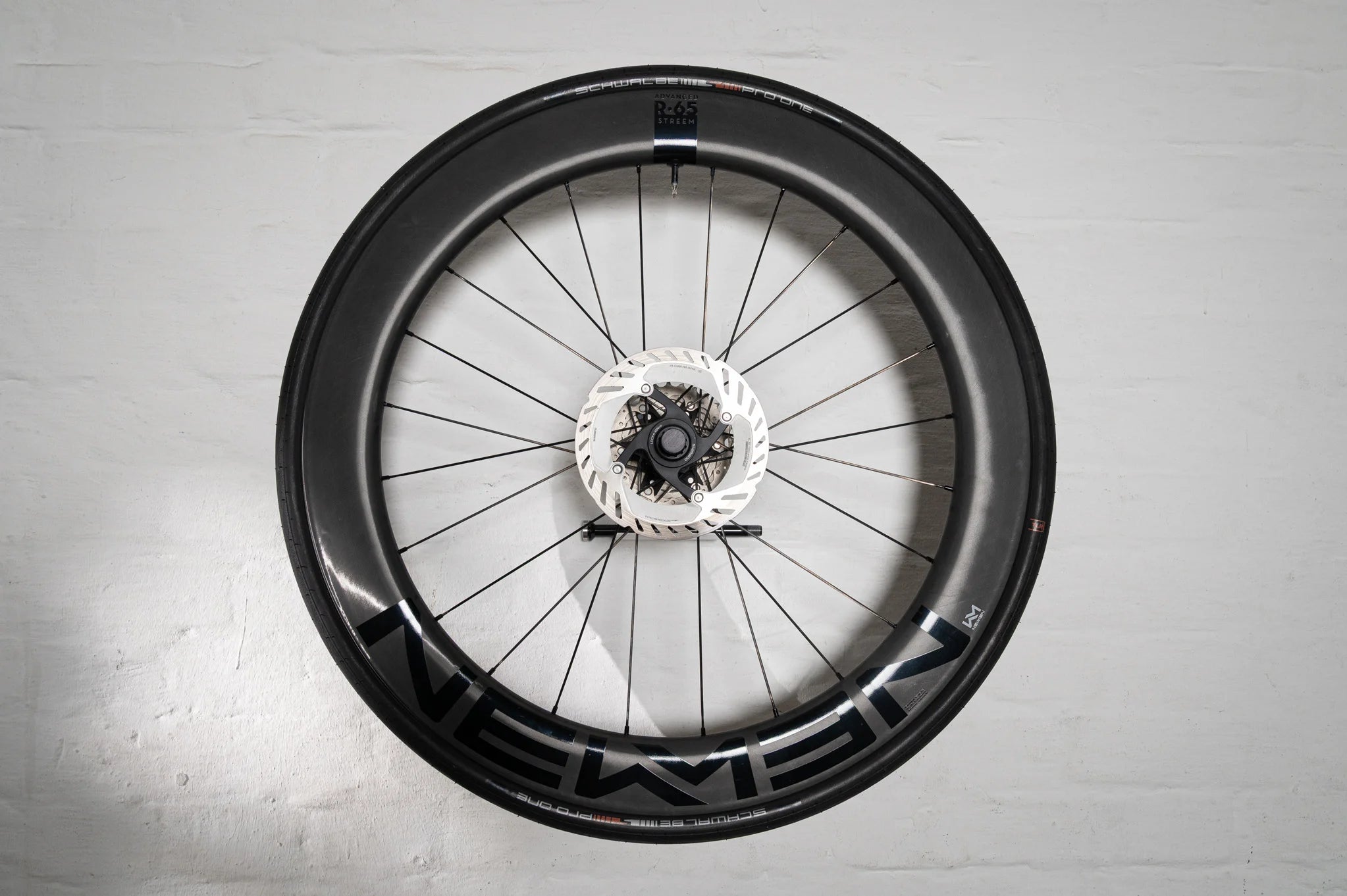 An aerodynamic carbon wheel securely mounted flush to a white wall using the Hold My Bike (HMB) wheel mount, turning high-end bike equipment into a modern piece of wall art.