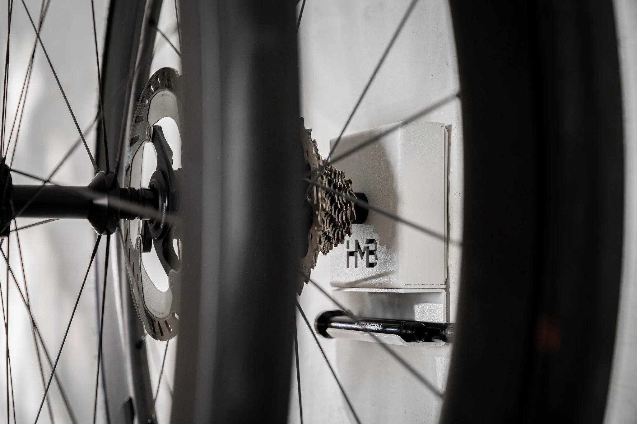 Close-up of the white Hold My Bike (HMB) wheel mount, securely holding a complete 12mm thru-axle wheelset on the wall thanks to the extra-long XL axle.