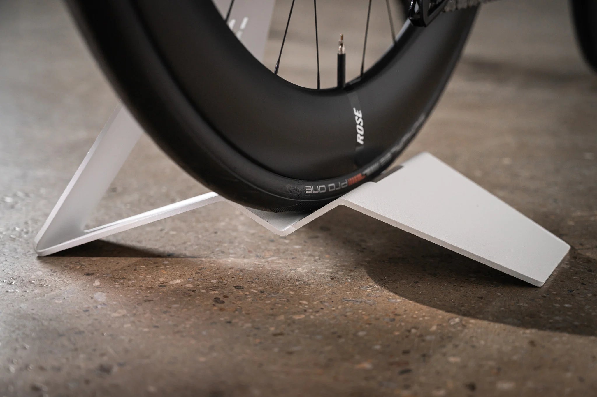 Detailed view of the precise tire cradle on the white Hold My Bike (HMB) bike stand, securely stabilizing a Rose road bike tire on the floor.