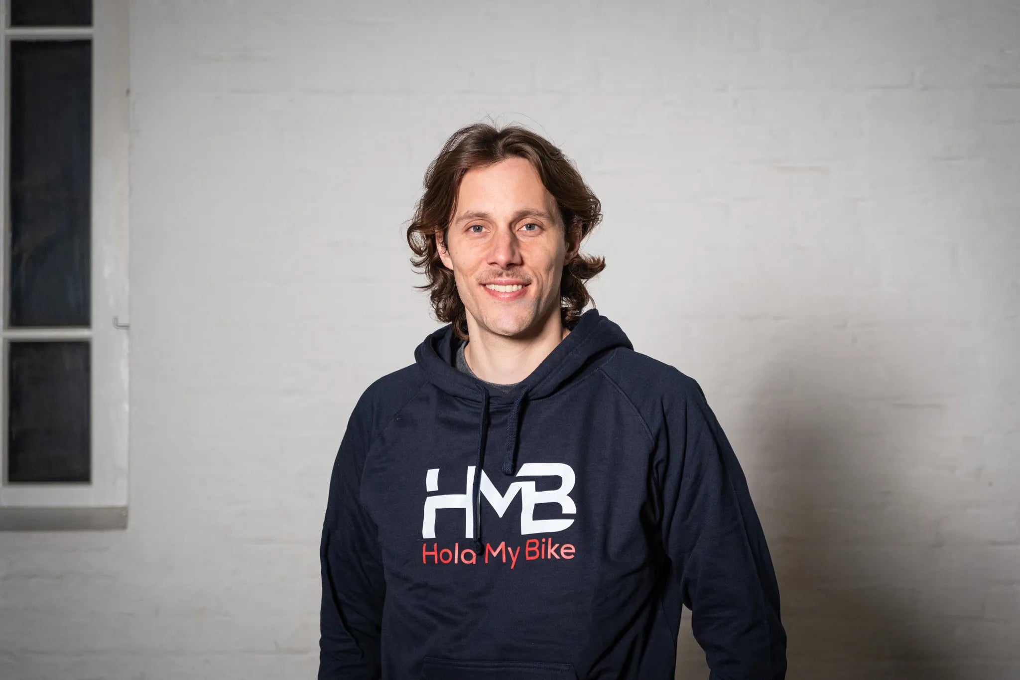 Hold My Bike (HMB) founder Michael Salomon wearing branded hoodies in front of a white brick wall – experts in bike wall mounts.
