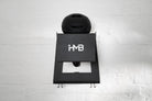Front-facing view of the matte black HMB Ultimate wall mount with a black cycling helmet on the top shelf, showcasing the laser-cut 'HMB' logo and integrated lower hooks for gear organization.