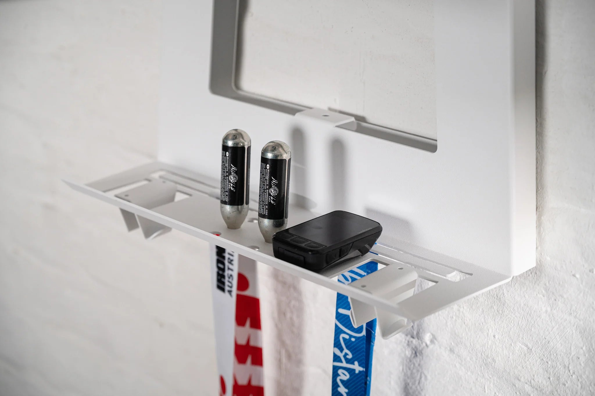 White Hold My Bike (HMB) Ultimate accessory shelf designed to organize bike computers and CO2 cartridges, featuring special cutouts to display race medals in your home.