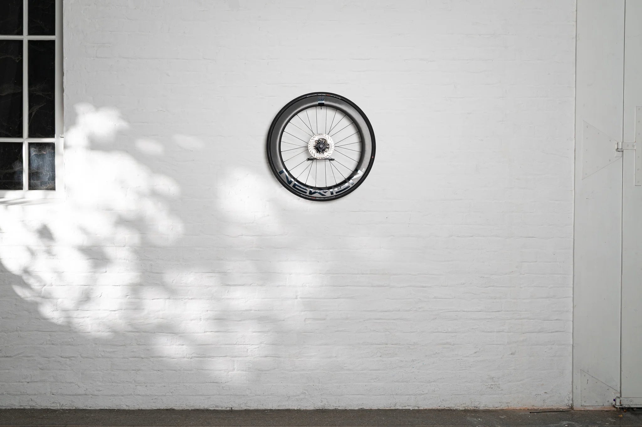 A carbon bike wheel mounted to the wall using the minimalist Hold My Bike (HMB) wheel mount, ideal for space-saving and stylish indoor storage in apartments.