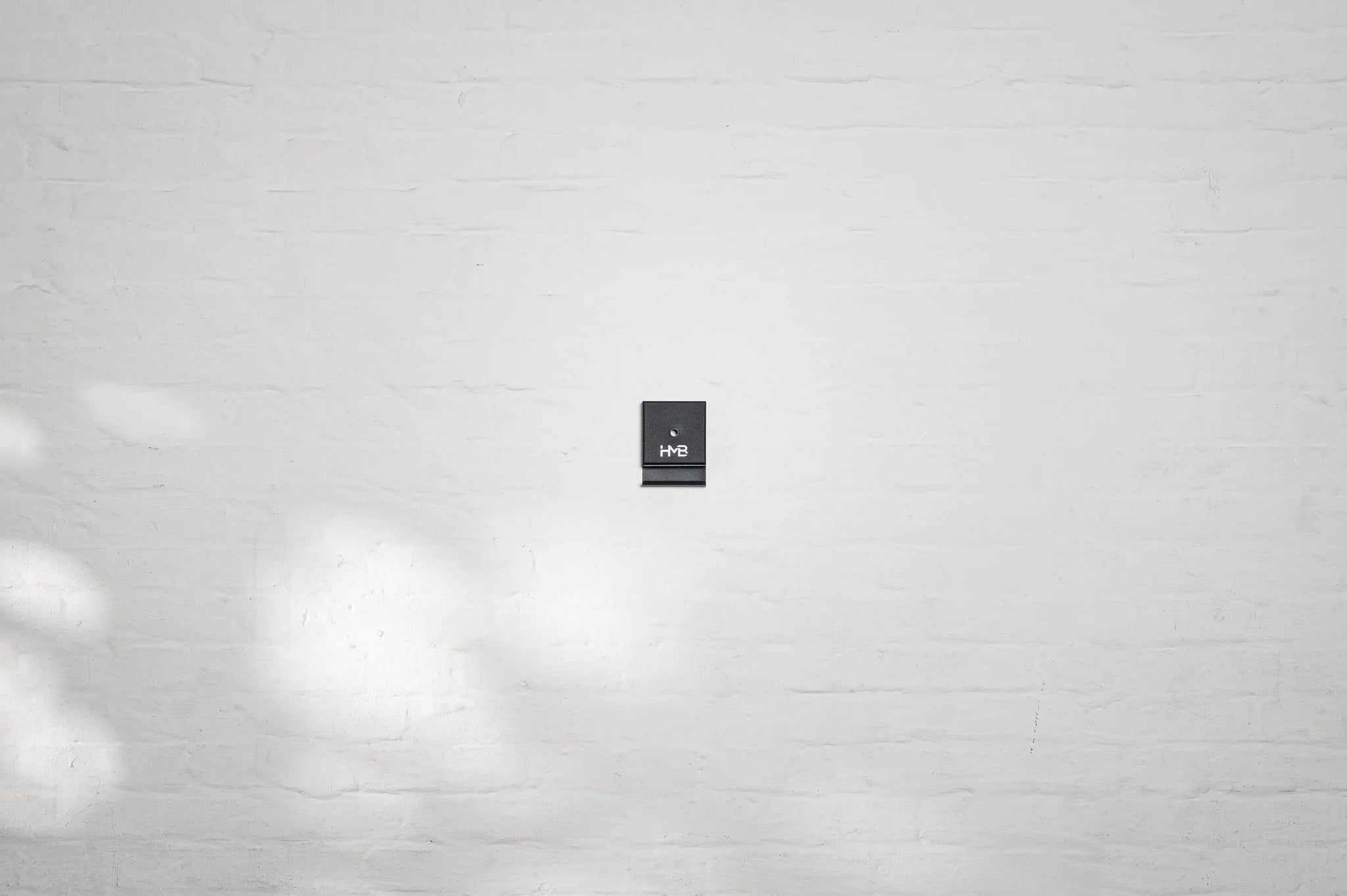 The minimalist black cover of the Hold My Bike (HMB) wheel mount, featuring an integrated shelf for the thru-axle and bold logo branding.