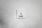 The minimalist white Hold My Bike (HMB) wheel mount featuring bold logo branding for a clean and modern indoor design.
