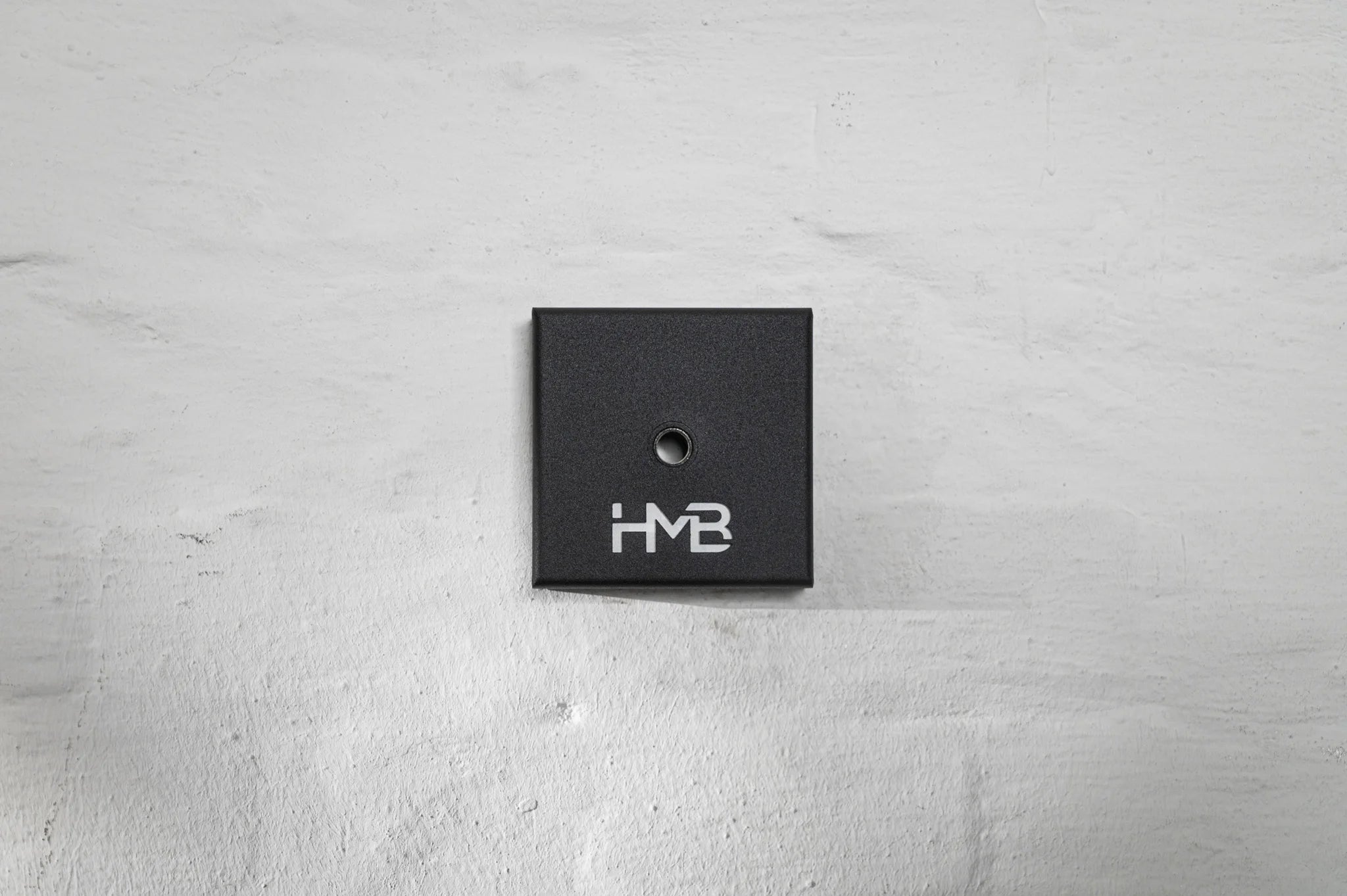 The elegant black Hold My Bike (HMB) wheel mount featuring subtle logo branding for aesthetic indoor bike wheel storage in your apartment.