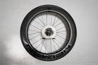 An aerodynamic carbon wheel securely mounted flush to a white wall using the Hold My Bike (HMB) wheel mount, turning high-end bike equipment into a modern piece of wall art.