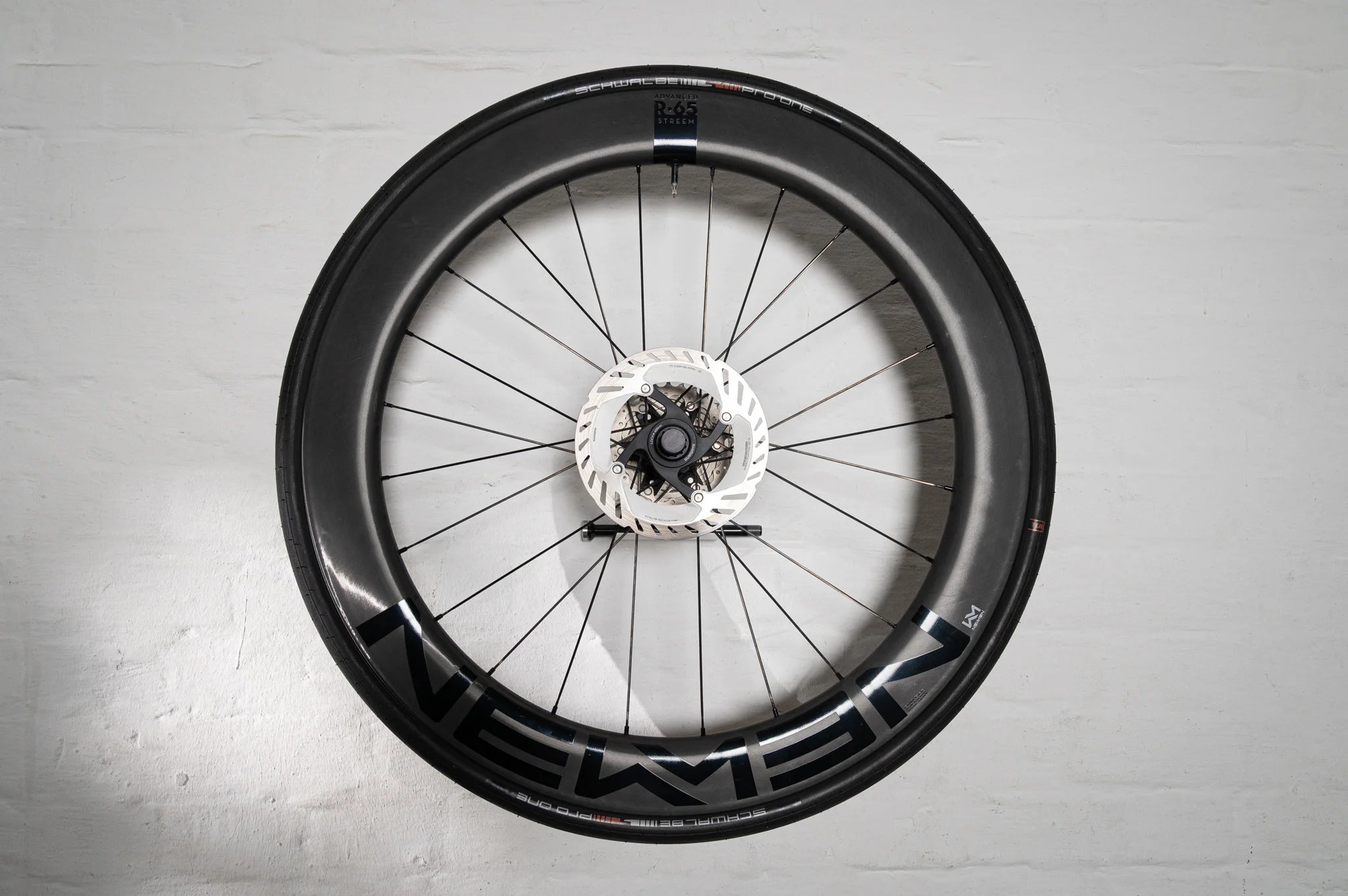 An aerodynamic carbon wheel securely mounted flush to a white wall using the Hold My Bike (HMB) wheel mount, turning high-end bike equipment into a modern piece of wall art.