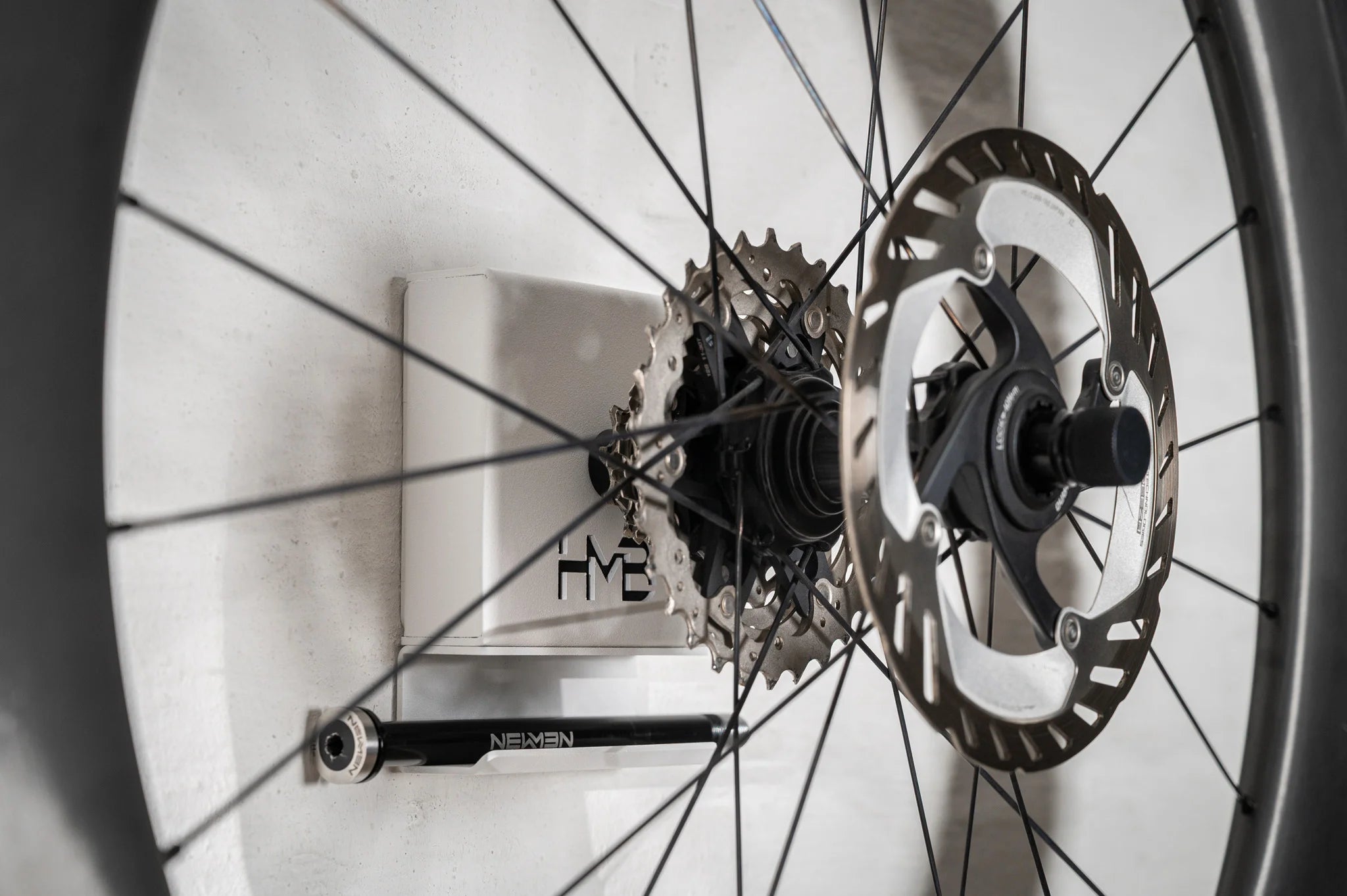 Close-up of the white Hold My Bike (HMB) wheel mount: A rear wheel with cassette and disc rotor is securely mounted, with the corresponding thru-axle neatly stored in the integrated shelf below the cover