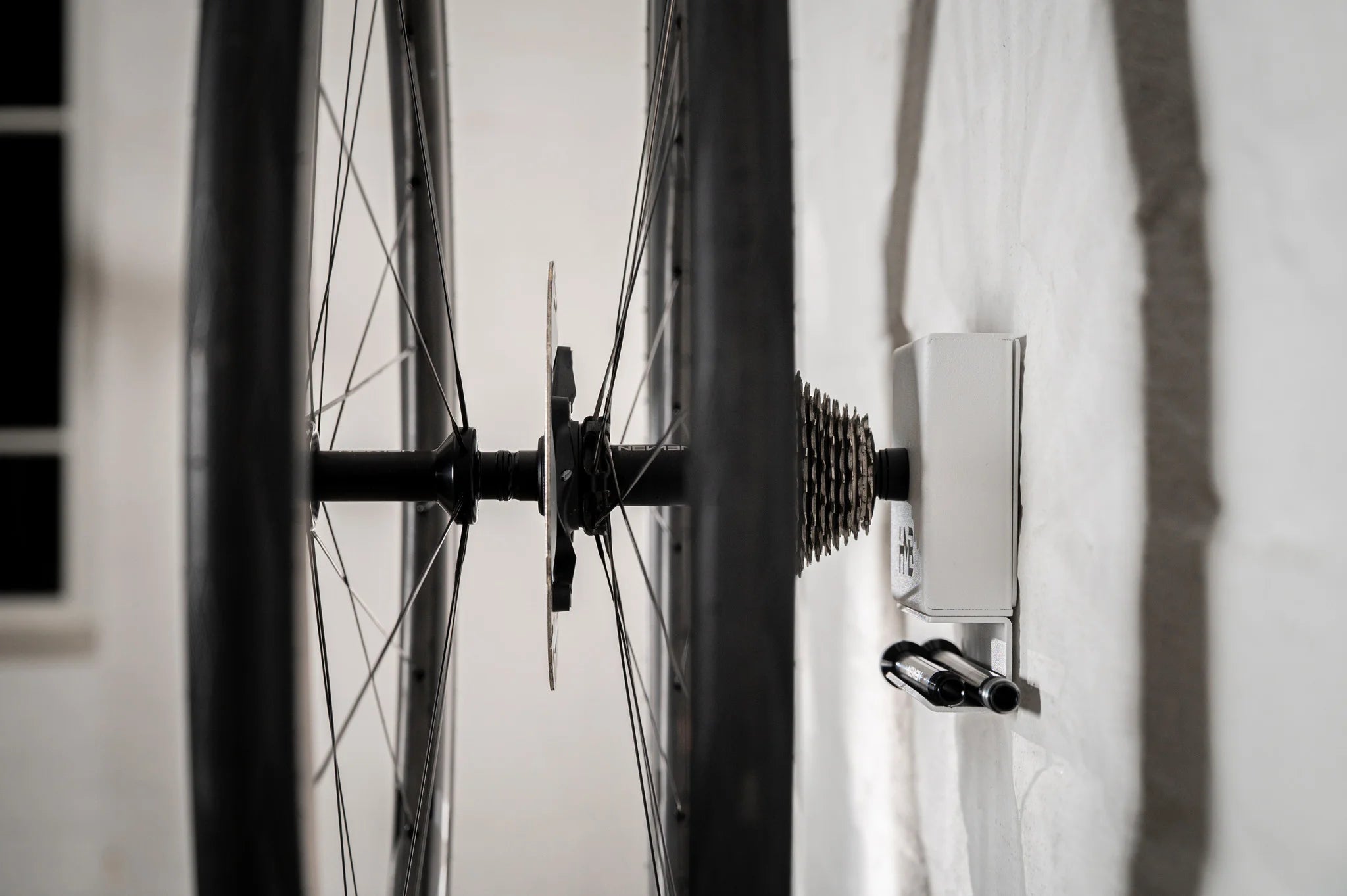 Side view of the white Hold My Bike (HMB) wheel mount: The extra-long XL version securely holds a full wheelset including the cassette, with two thru-axles neatly stored in the integrated shelf below.