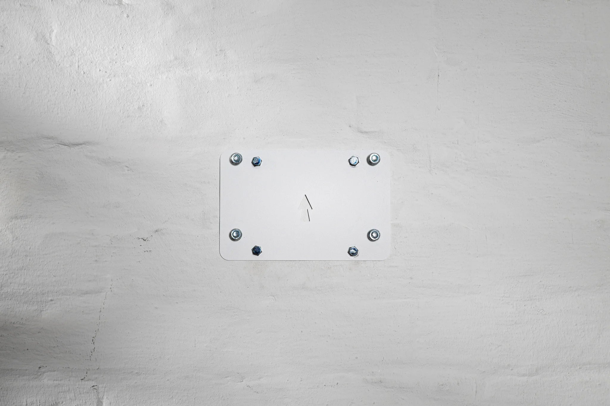 A white HMB easy Mounting System base plate bolted to a brick wall, featuring an upward arrow indicator for correct orientation and a clean, hidden-fastener look