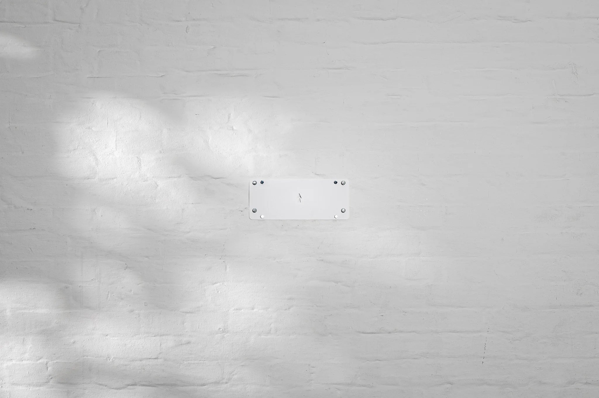 Centered shot of the HMB easy mounting system base plate installed on a white brick wall, featuring a laser-cut orientation arrow and four secure mounting points for the HMB minimal wall mount