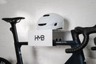 A close-up view of a matte black Canyon Aeroad CF SLX road bike stored on a white HMB Minimal wall mount, featuring a white helmet on the top shelf and integrated slots holding two CO2 cartridges.