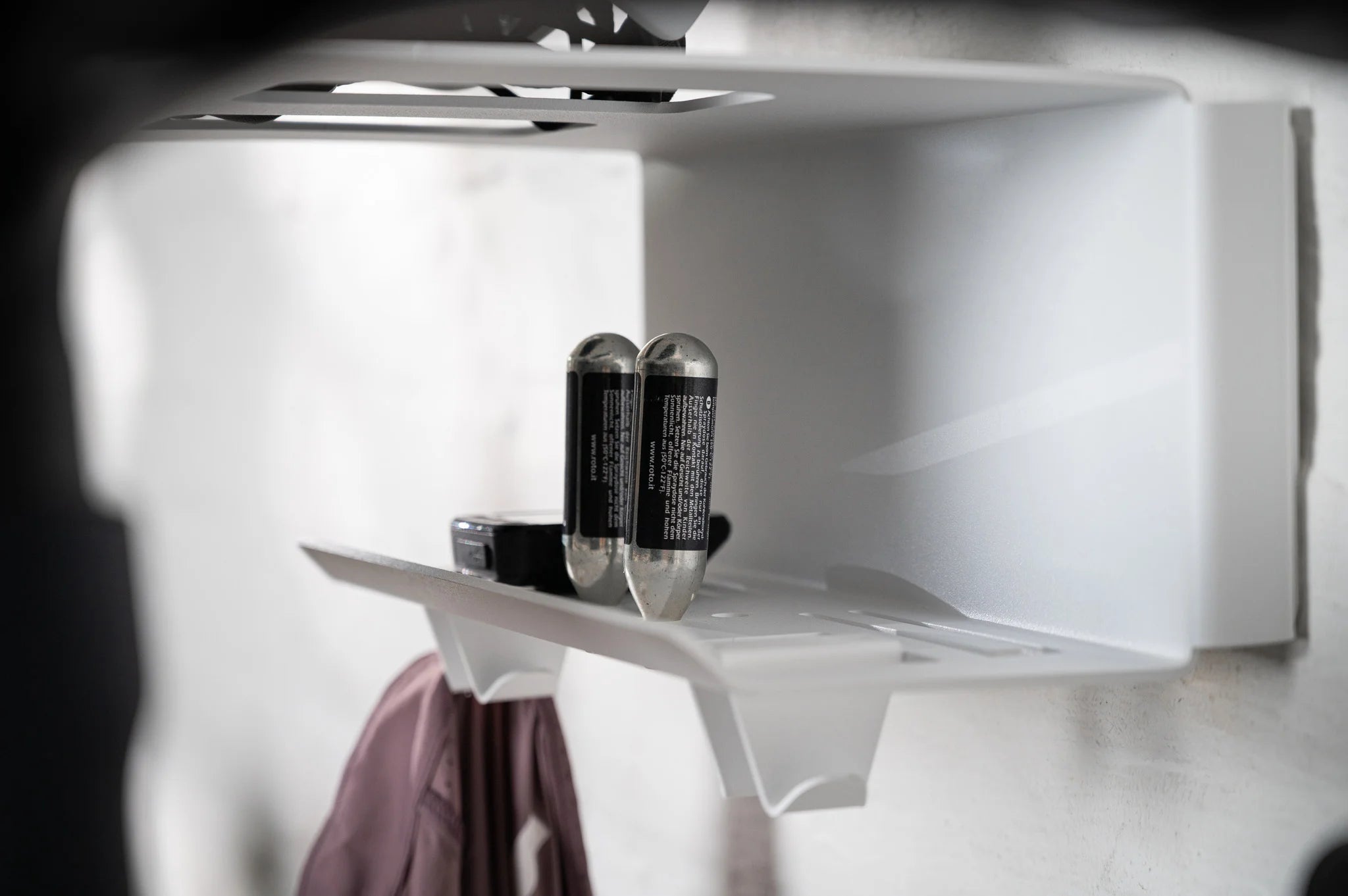 Close-up of the integrated accessory shelf on the white HMB Ultimate wall mount, organizing two CO2 cartridges and a bike computer above the lower gear hooks.