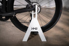 Front view of the white Hold My Bike (HMB) Bike Stand: Features a sleek A-frame design with a laser-cut HMB logo, ideal for modern home interiors.