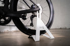 Detailed close-up of the white Hold My Bike (HMB) bike stand, securely holding a Rose road bike by the rear axle without touching the frame or spokes.