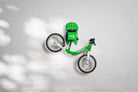 A green Hold My Bike (HMB) Kids wall mount securely holding a green woom 1 balance bike by the seat post, with a matching green woom helmet resting on the integrated top shelf.