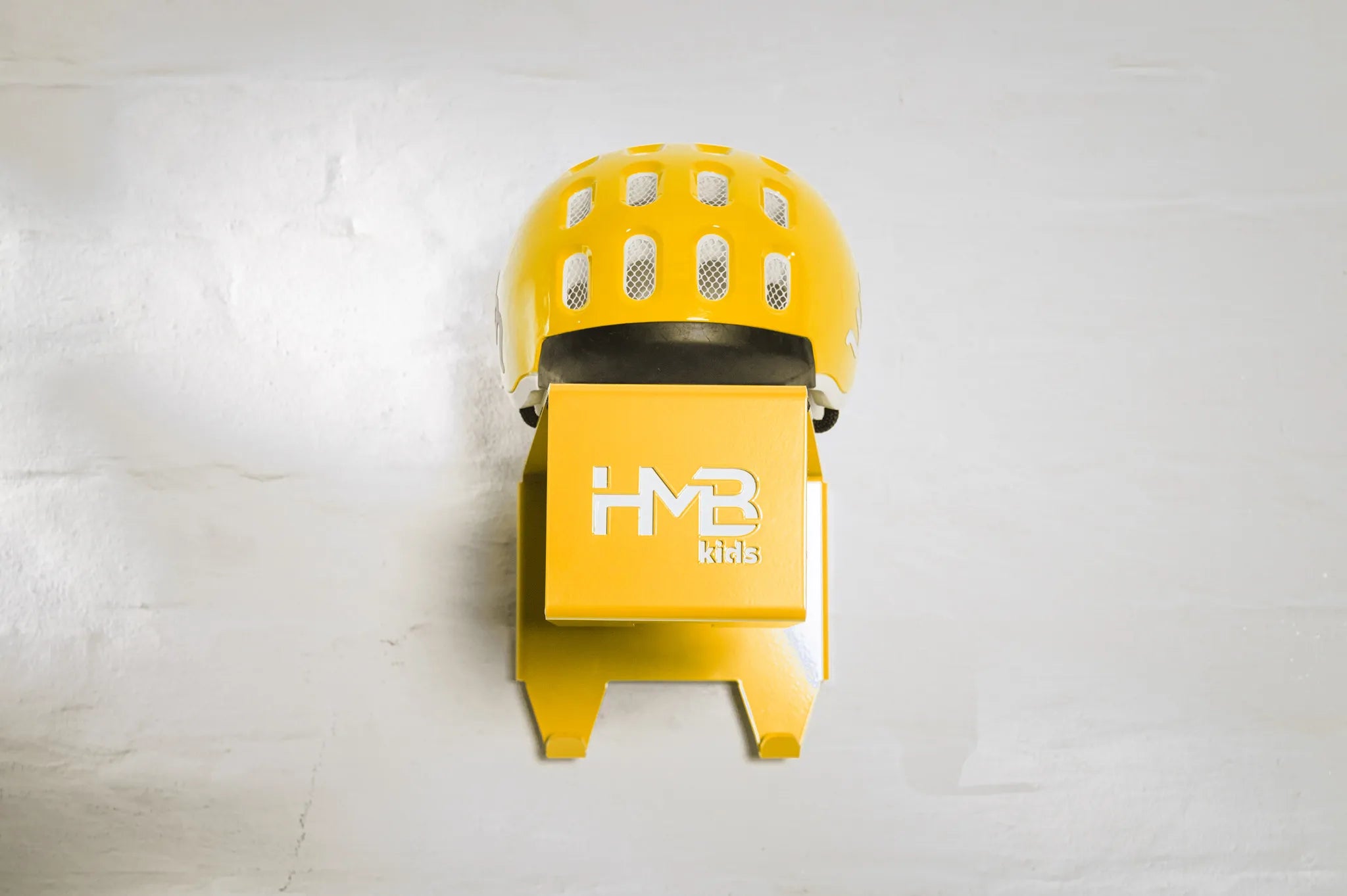Front view of a ryellowHold My Bike (HMB) Kids wall mount with a matching yellow woom helmet resting on the top shelf, showcasing the laser-cut branding and two integrated hooks for cycling gear.