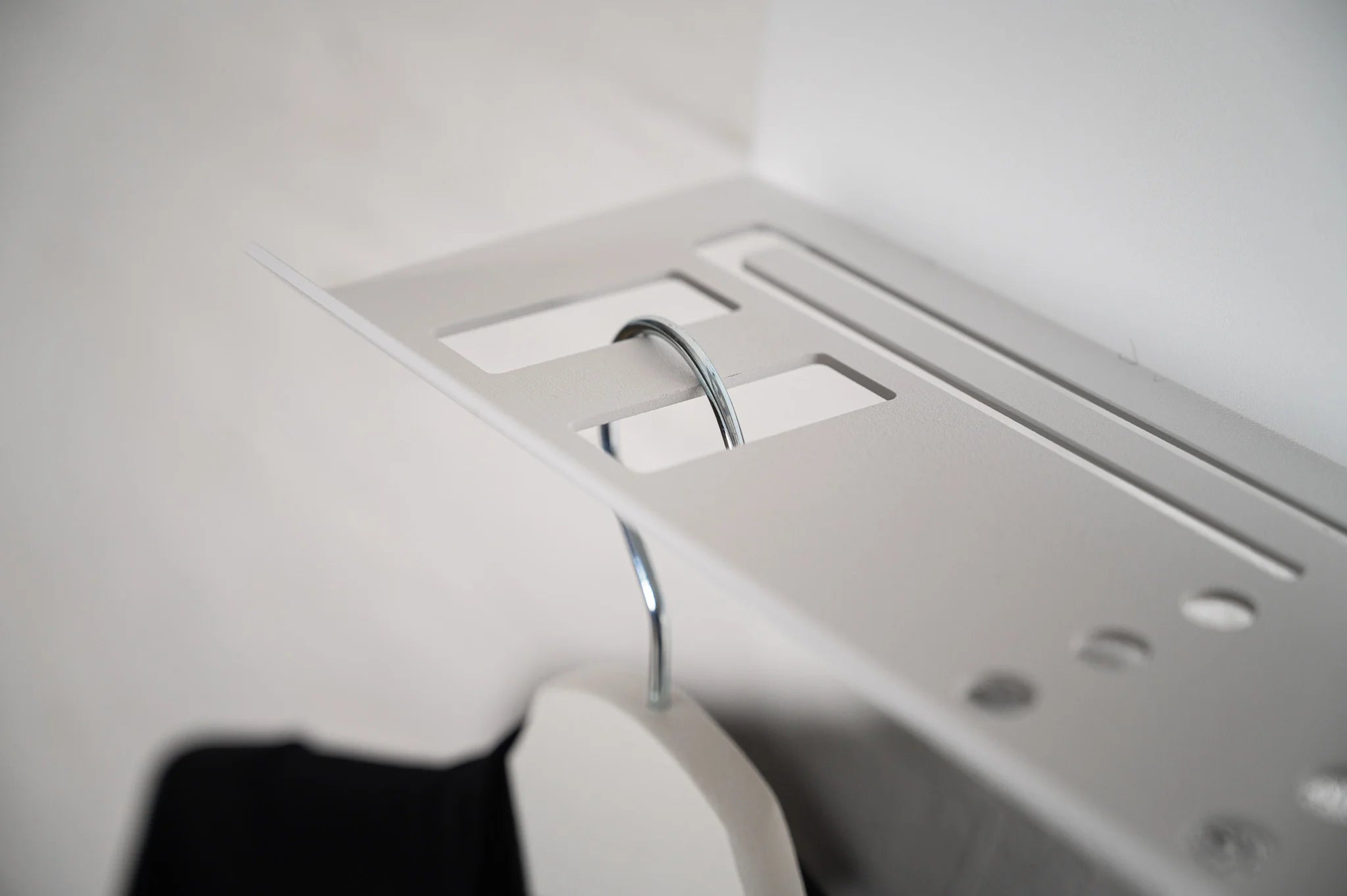 Close-up of the Hold My Bike (HMB) indoor bike wall mount featuring integrated slots for clothes hangers to keep cycling apparel organized in your apartment.