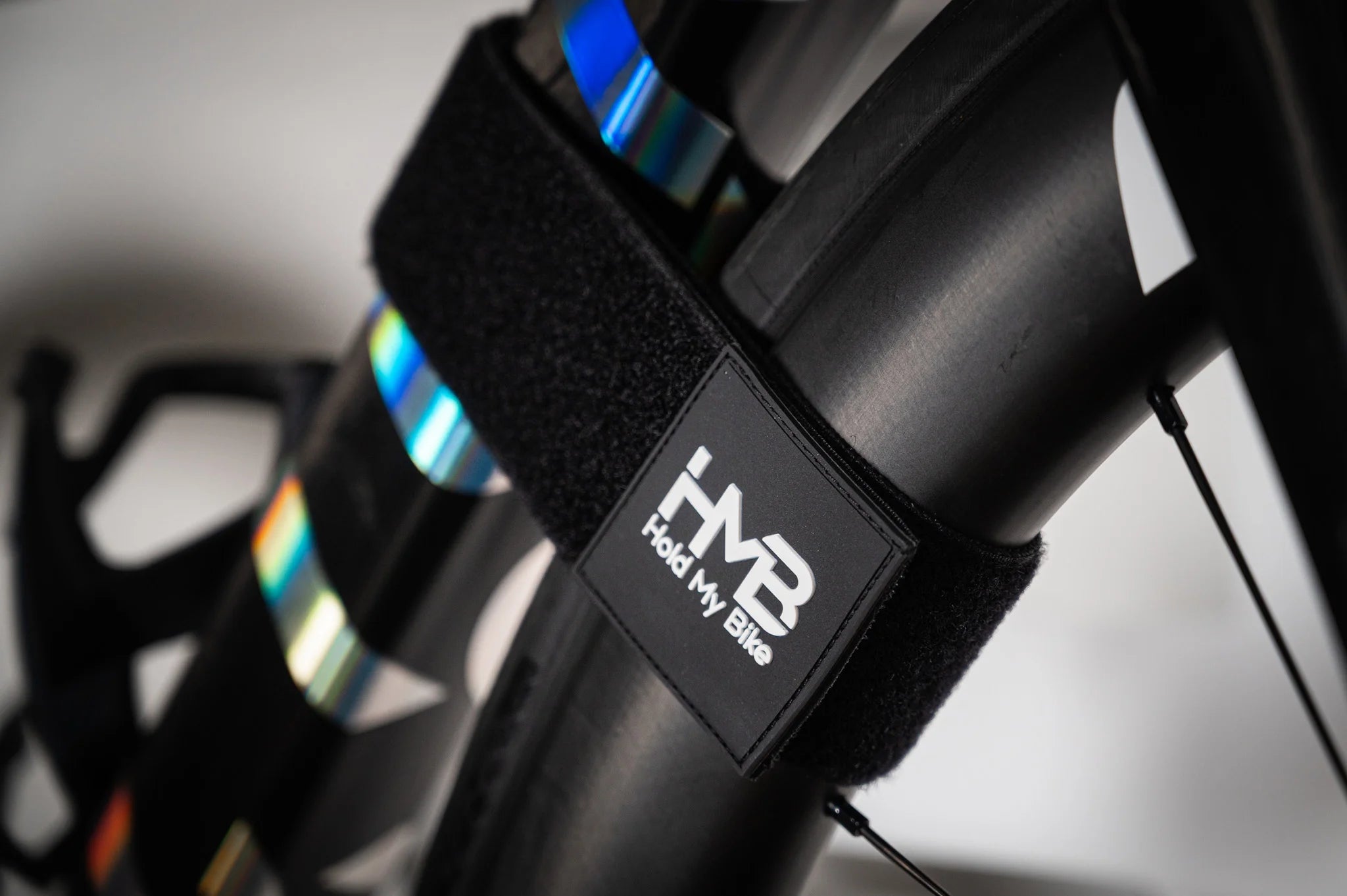 Close-up of the black HMB Wheel Strap with a white logo badge, securely fastening a bicycle's front wheel and frame together to prevent movement while stored on a wall mount.