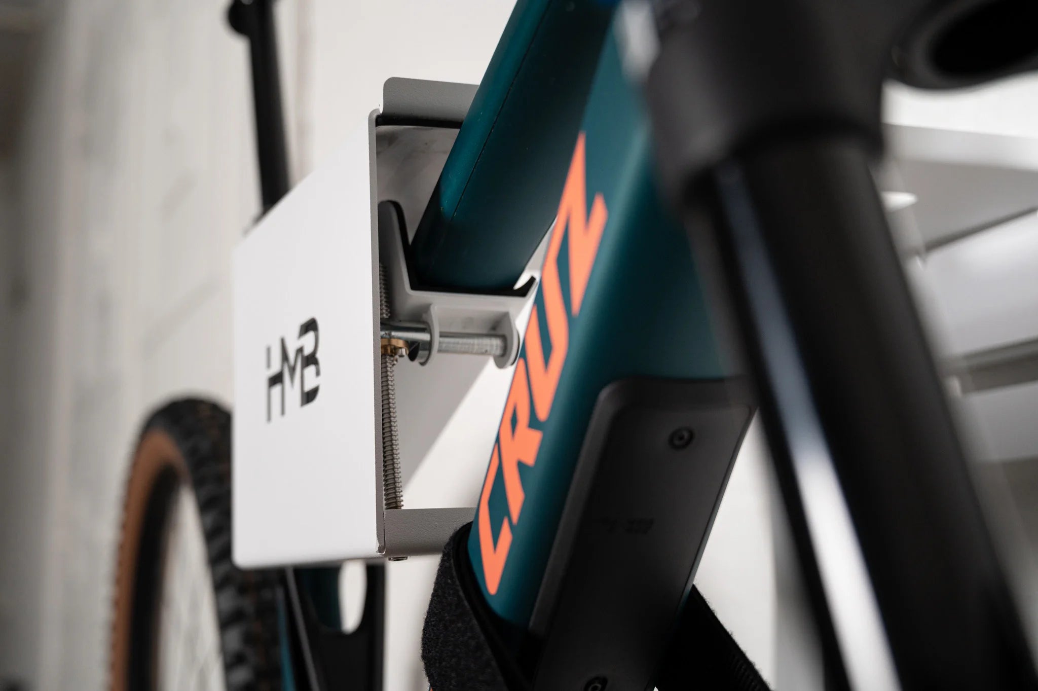 Close-up of a Santa Cruz mountain bike secured in the white HMB Ultimate XL wall mount, showing the innovative tilt mechanism and threaded adjustment rod used to level the bike's frame.