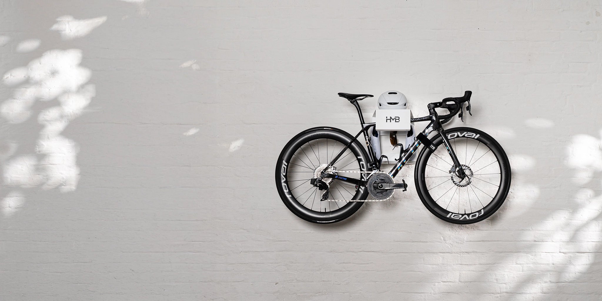Hold My Bike innovative white wall-mounted bike rack with integrated storage for helmet and gear, featuring a black road bike on a light brick wall