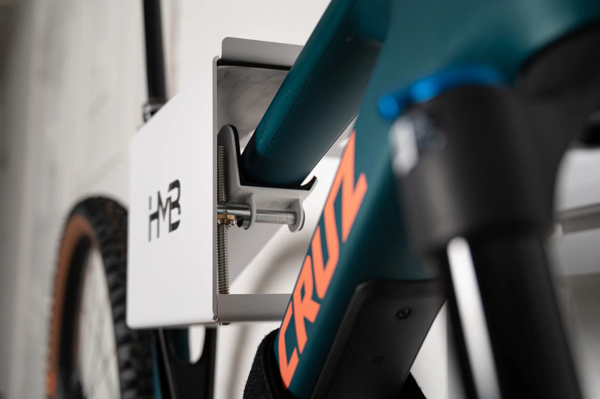 Close-up of a Santa Cruz mountain bike secured in the white HMB Ultimate XL wall mount, highlighting the innovative tilt mechanism and threaded adjustment rod used to level the bike's frame.